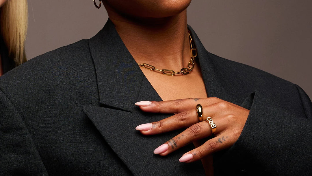 Gold chain necklace and statement rings on woman in black blazer, modern jewellery