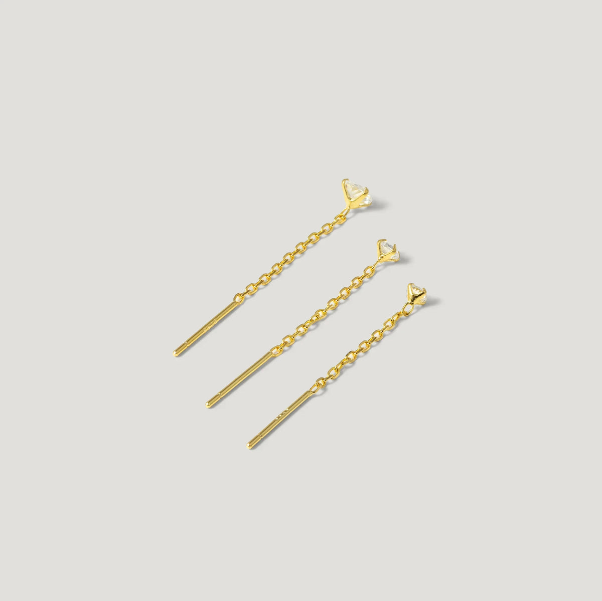 Three gold chain drop earrings with heart-shaped studs on a light grey background