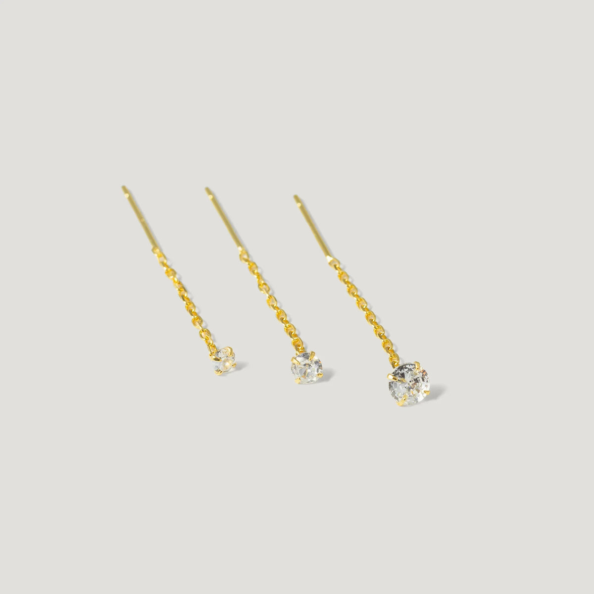 Three gold chain threader earrings with round clear gemstones on a white background