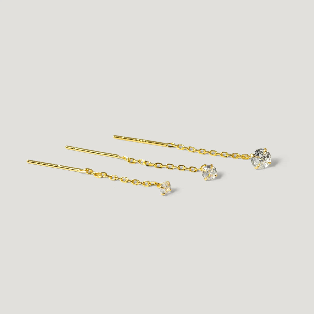 Three gold chain threader earrings with clear gemstone studs on a light background