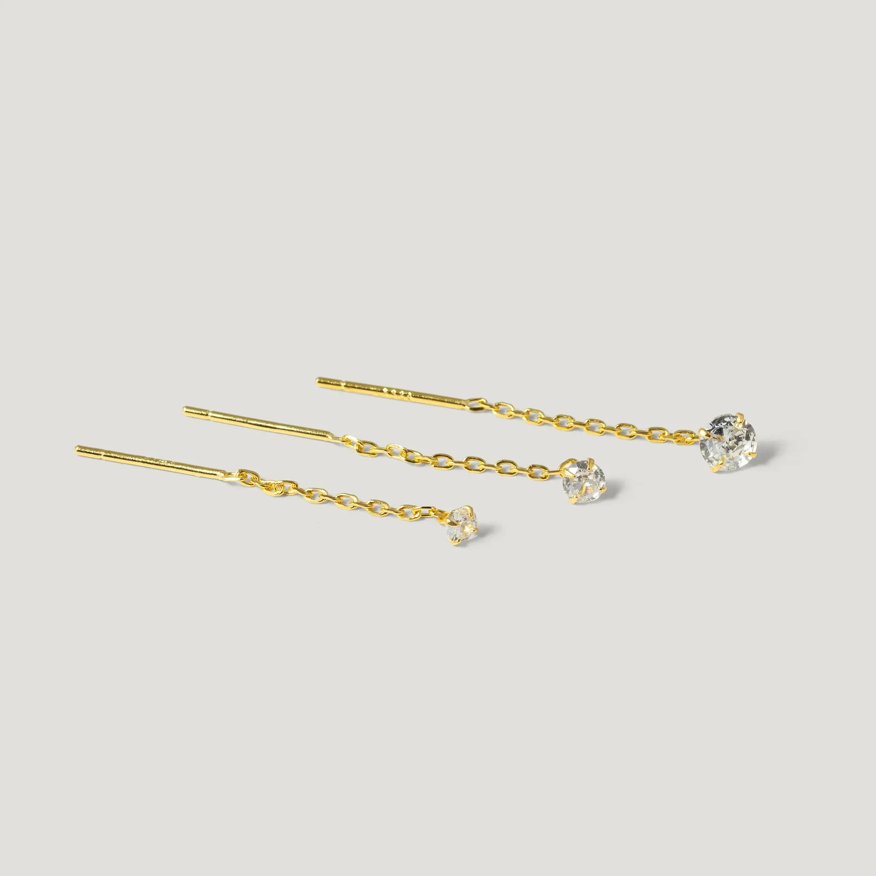 Three gold chain threader earrings with clear gemstone studs on a light background