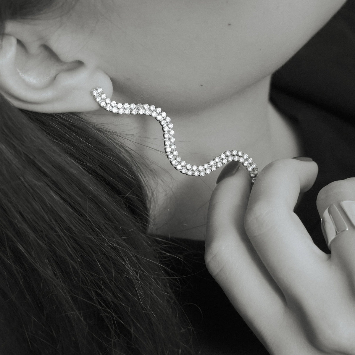 Elegant wavy diamond ear cuff earring on woman's ear, modern jewelry close-up