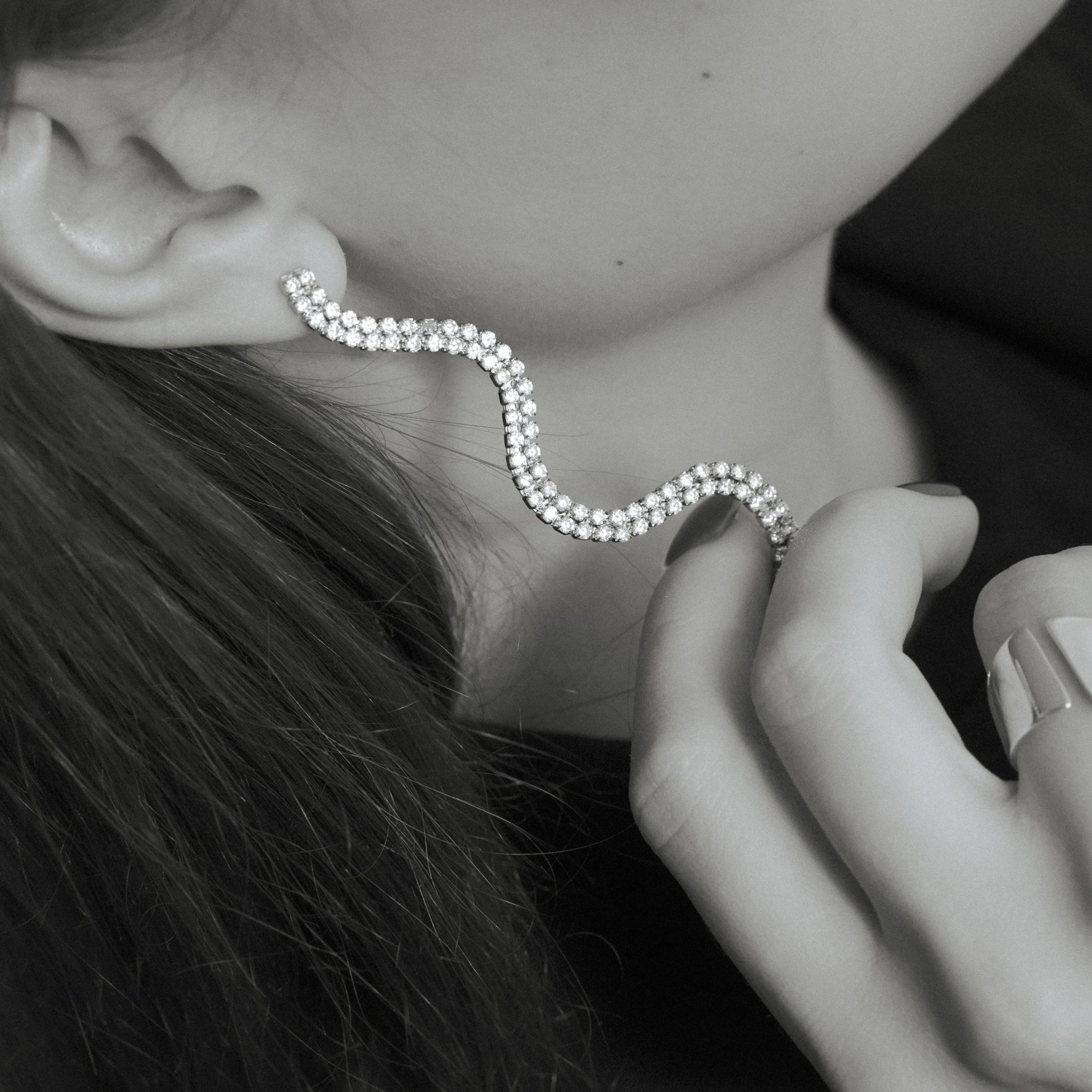 Elegant wavy diamond ear cuff earring on woman's ear, modern jewelry close-up