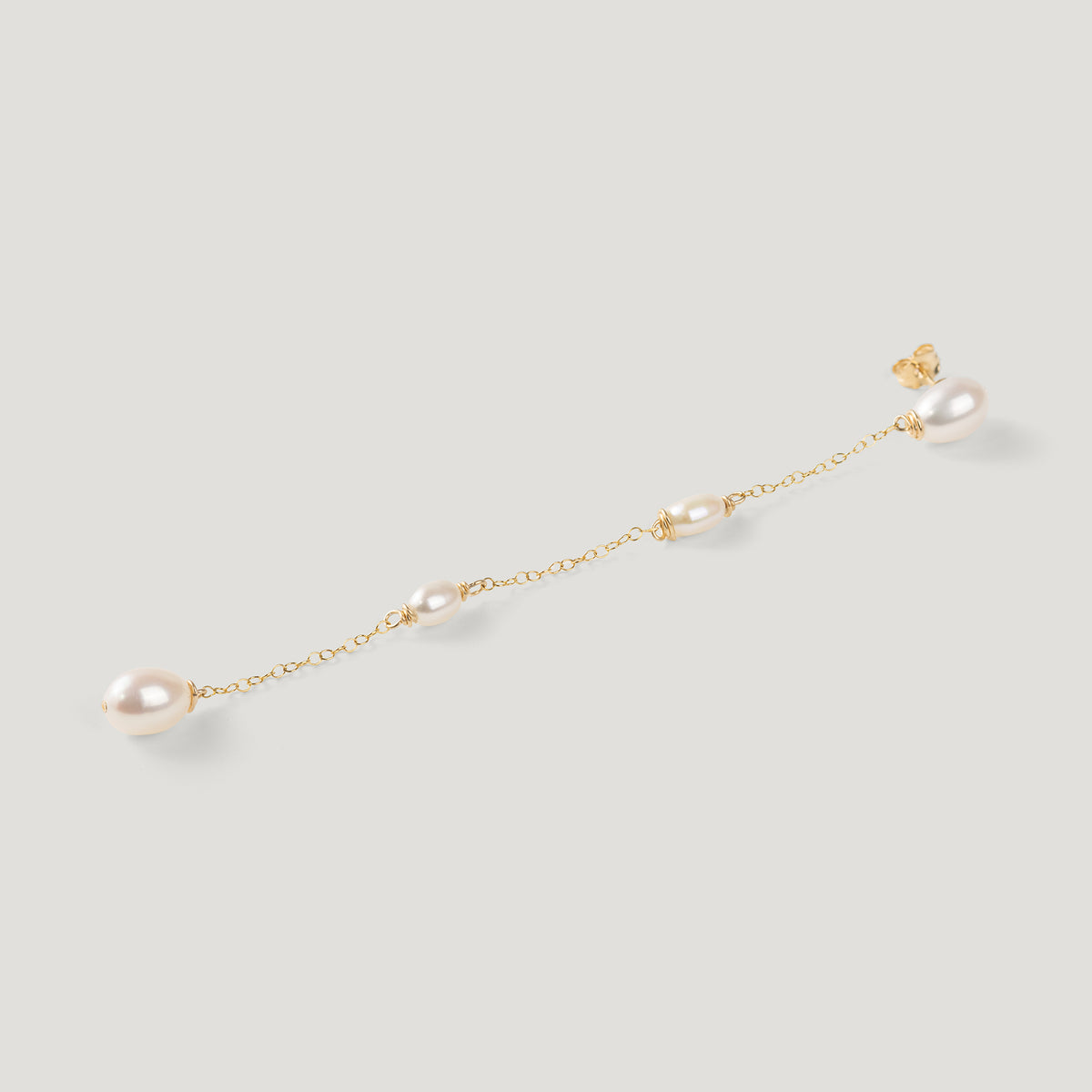 Single gold pearl chain earring laid diagonally, showing stud and dangling pearls.