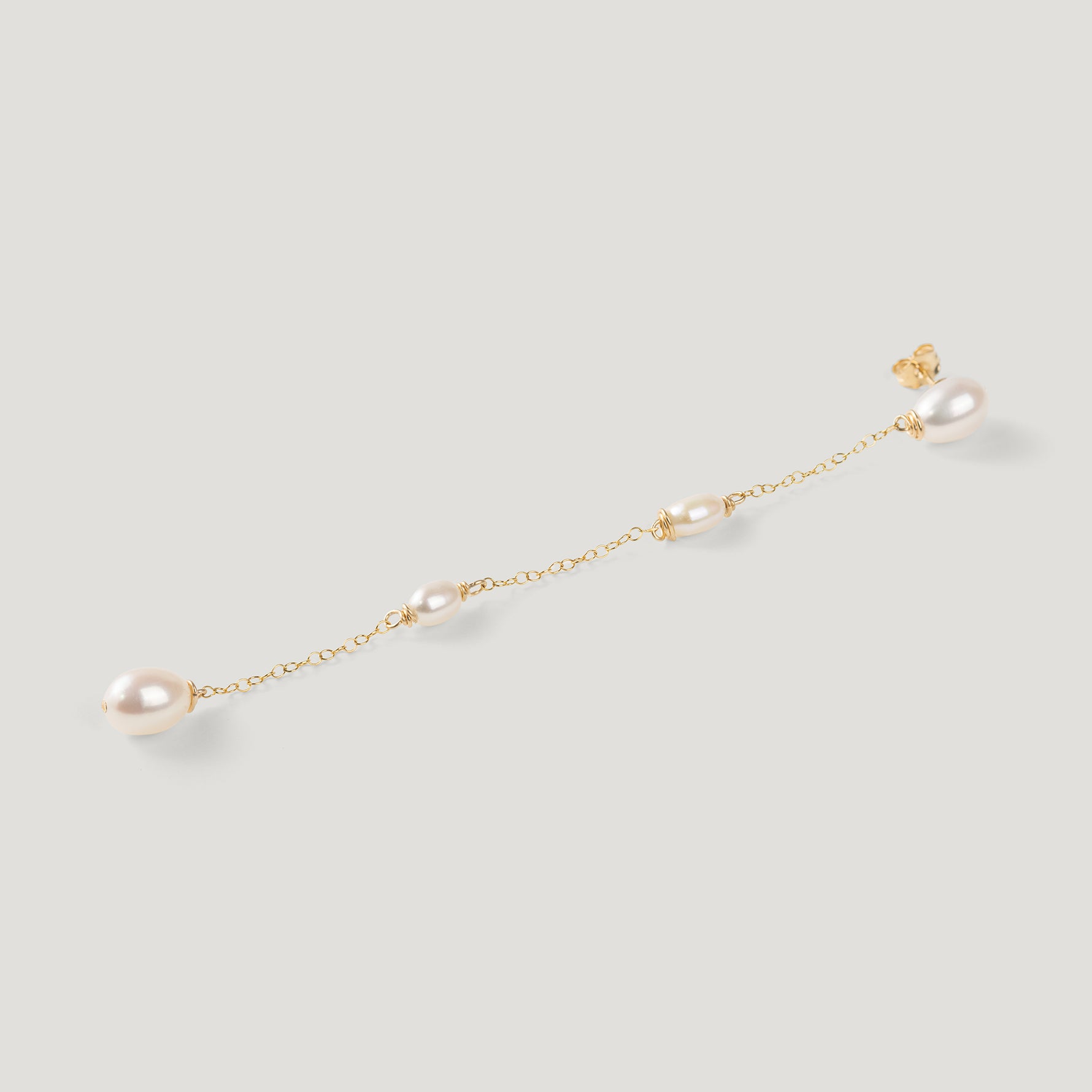 Single gold pearl chain earring laid diagonally, showing stud and dangling pearls.