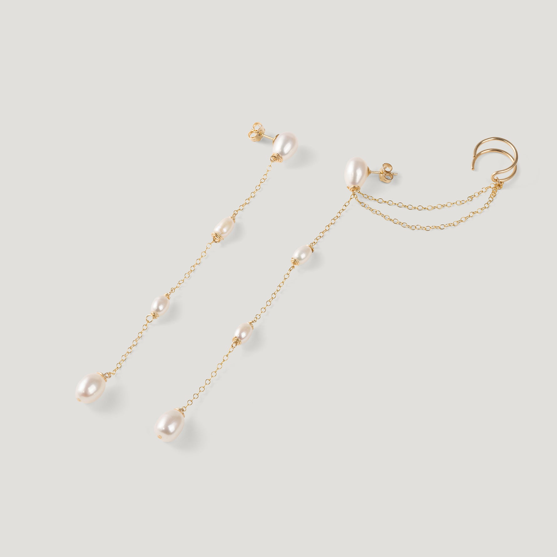 Pair of gold pearl chain earrings spread apart, ear cuff design clearly visible.