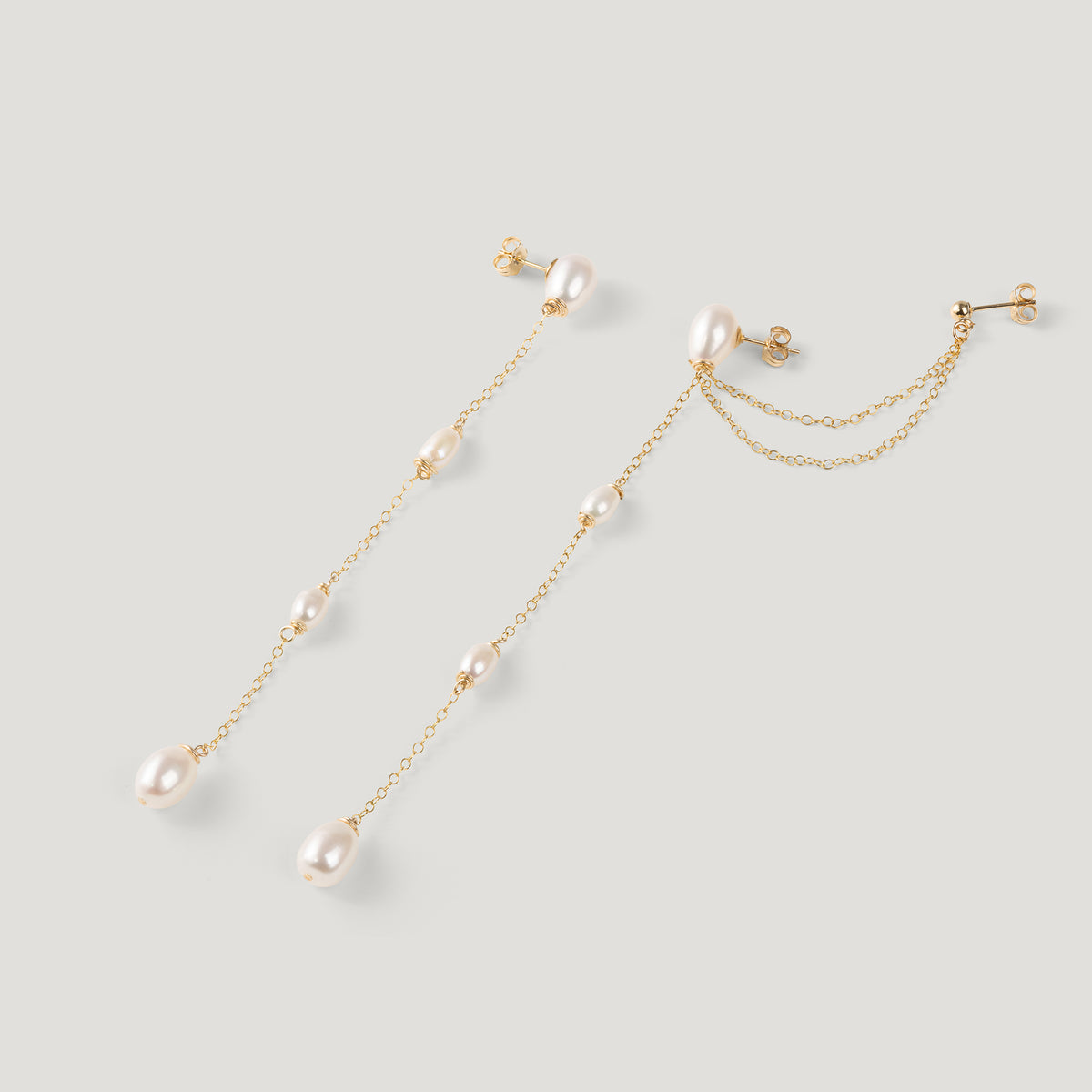 Pair of gold pearl chain earrings at an angle, showing ear cuff and earring backs.