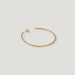 Single gold hoop earring, thin polished band, laid on light background.