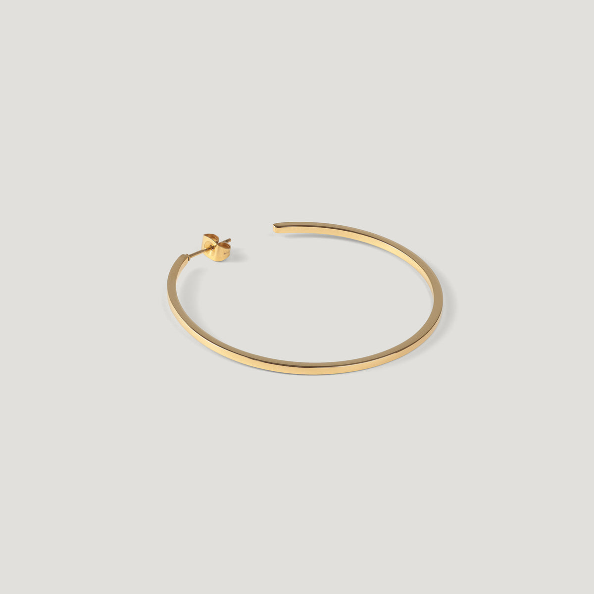 Single gold hoop earring, thin polished band, laid on light background.