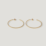Pair of thin gold hoop earrings standing upright side by side on light background.