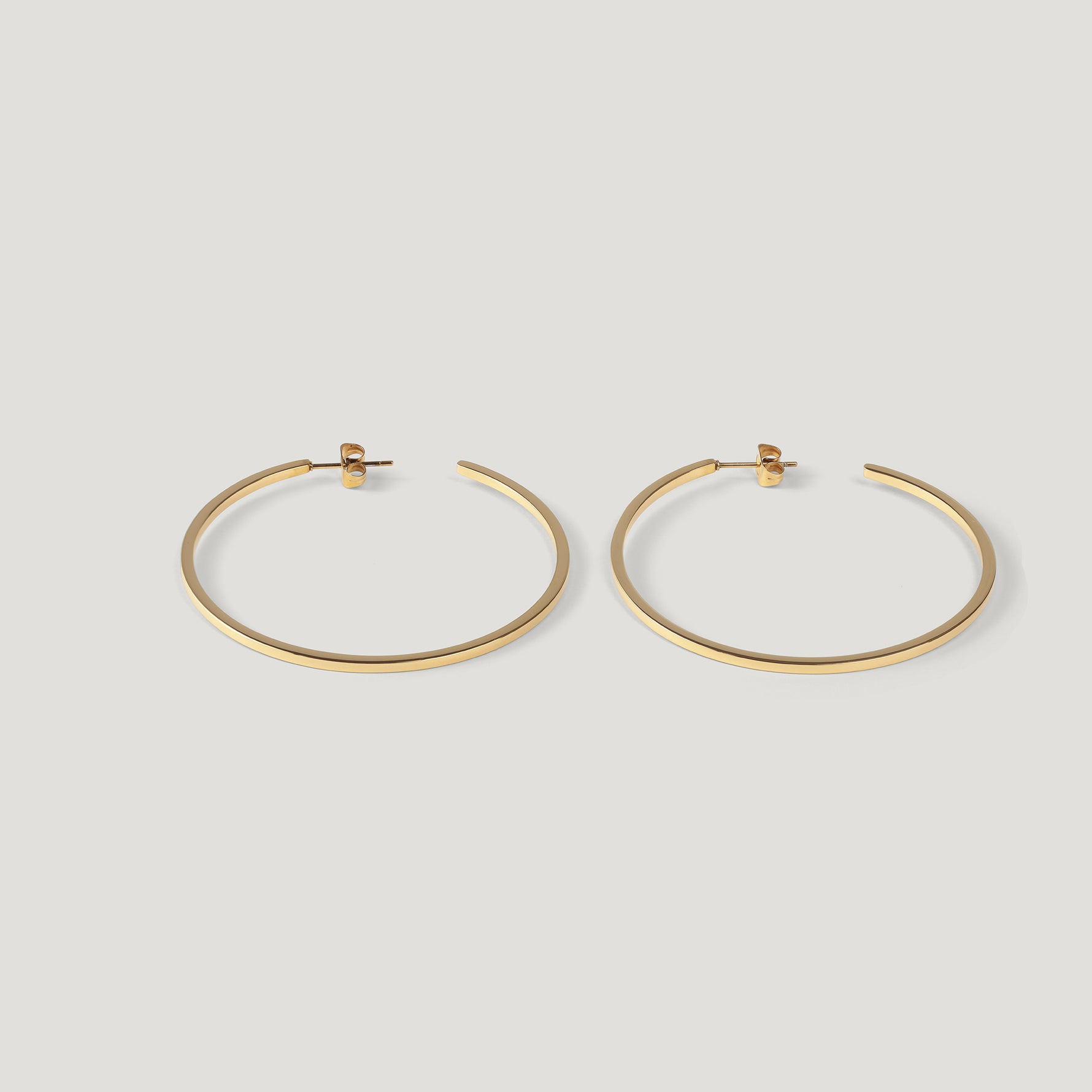 Pair of thin gold hoop earrings standing upright side by side on light background.
