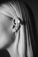 Close-up of ear wearing multiple silver earrings and ear cuff with chain details