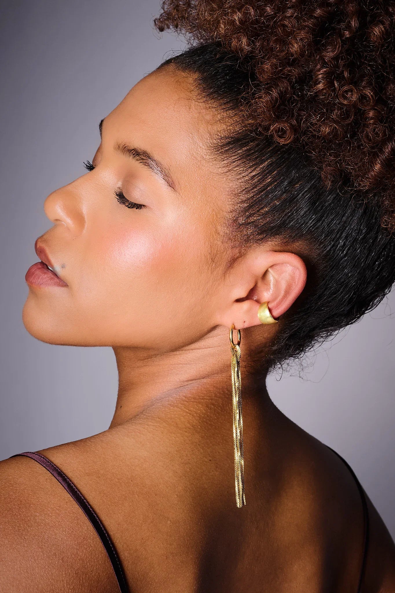 Woman wearing long gold statement earring and gold ear cuff, side profile