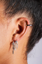 Close-up of an ear with multiple silver hoop earrings and dangle charms, minimalist style