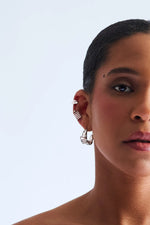 Woman wearing silver sculptural hoop earrings and ear cuffs against light background