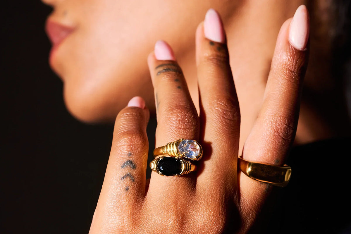 Close-up of hand with gold rings set with clear and black stones, pink manicure, tattoos
