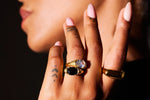 Close-up of hand with gold rings set with clear and black stones, pink manicure, tattoos