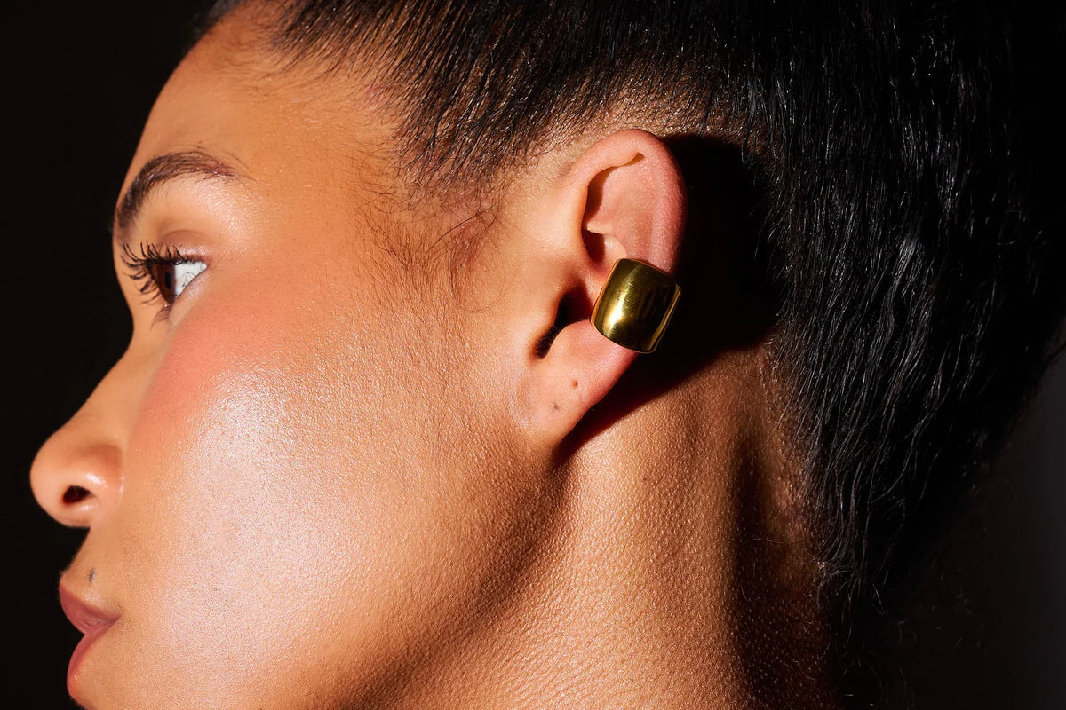 Close-up of a woman wearing a chunky gold ear cuff earring against a dark background