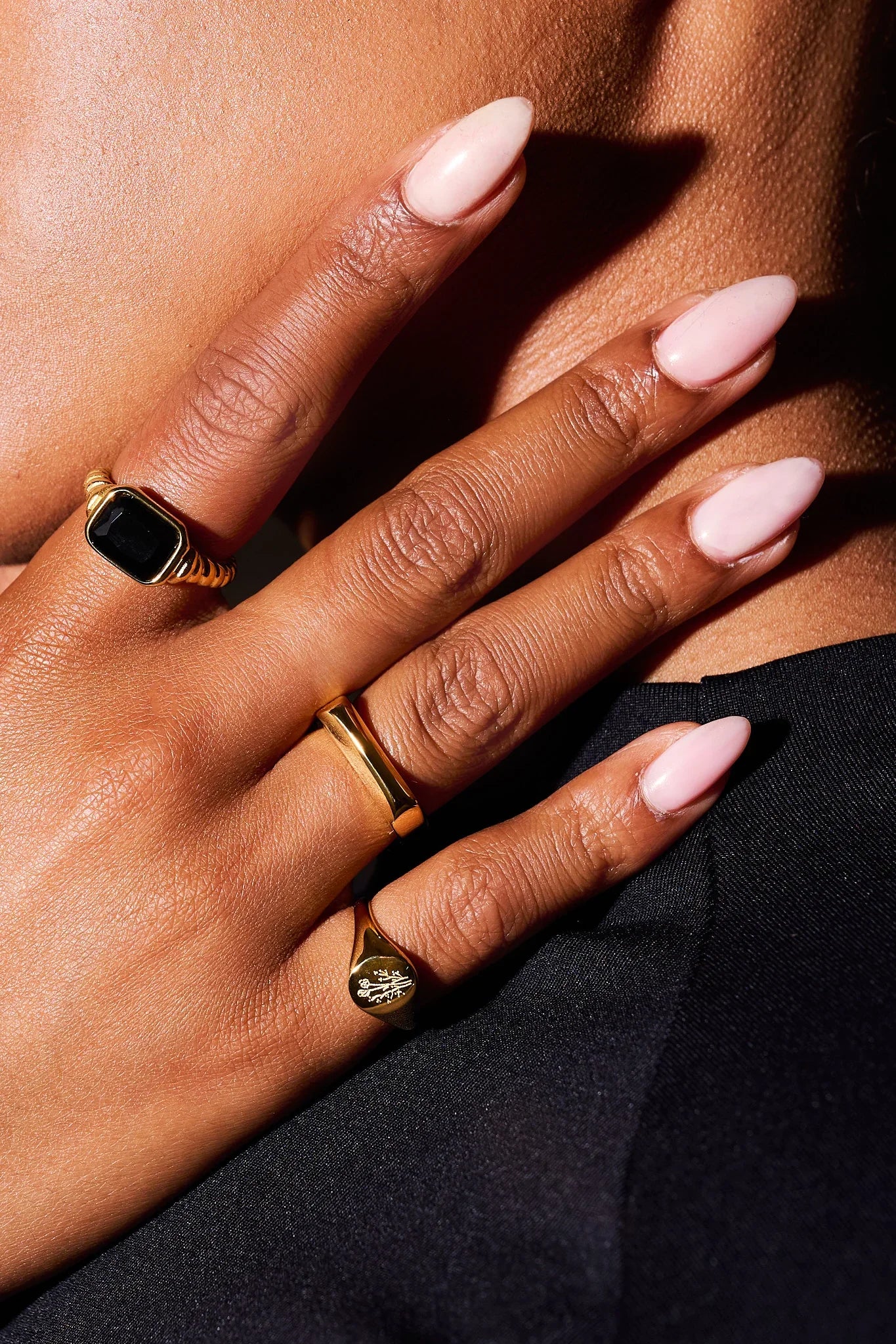 Hand with pink manicured nails wearing three stylish gold rings, one with a black stone