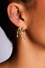 Gold hoop earrings with dangling spike and chain accents worn on ear