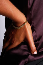 Elegant gold chain bracelet on wrist against deep purple satin fabric