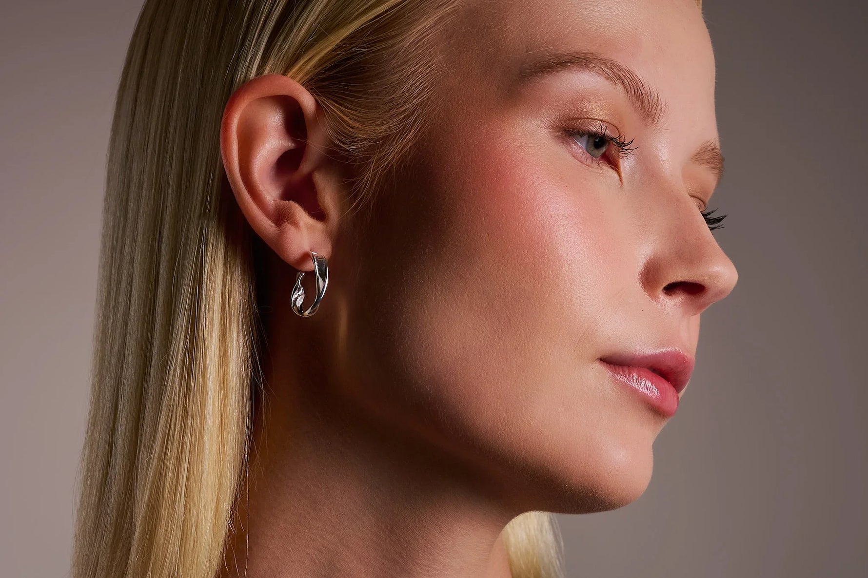 Woman wearing a silver twisted hoop earring, close-up on ear and jewelry