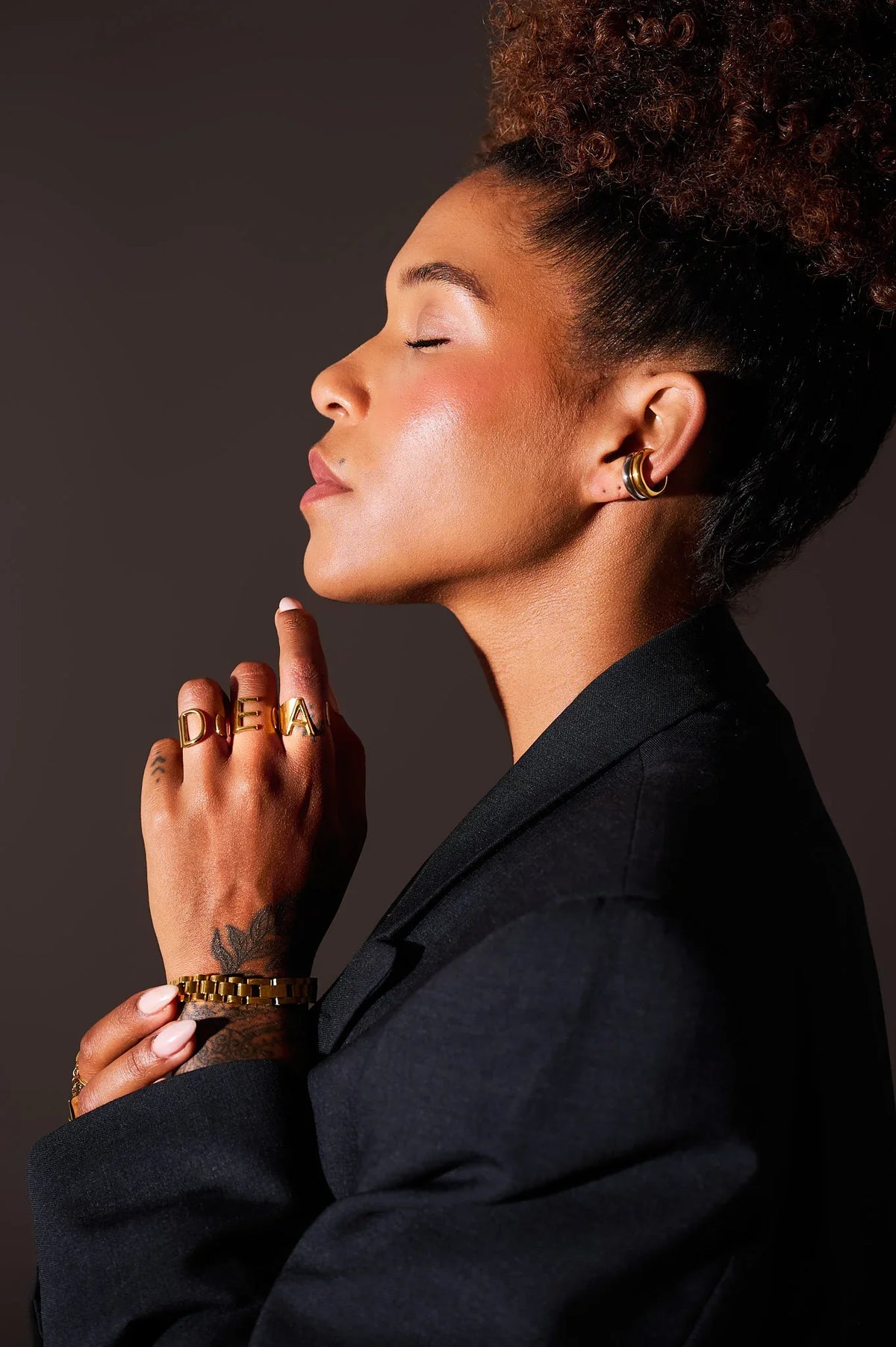Woman wearing gold statement rings, hoop earrings, and a gold bracelet, profile view