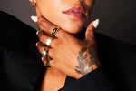 Close-up of a hand with gold rings and tattoos, wearing a black blazer, elegant jewellery style