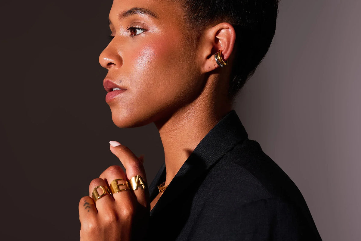Woman wearing gold statement ear cuff and bold gold letter rings on hand
