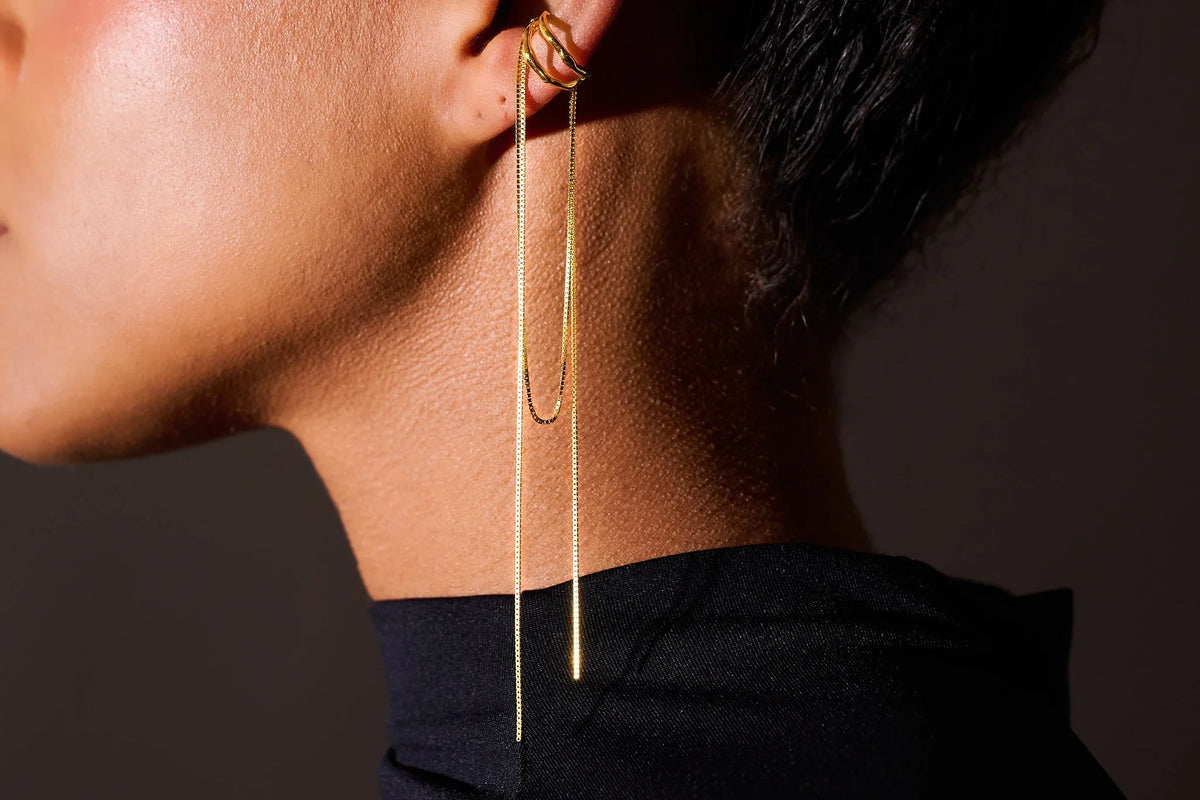Gold ear cuff earring with long delicate chains on model's ear