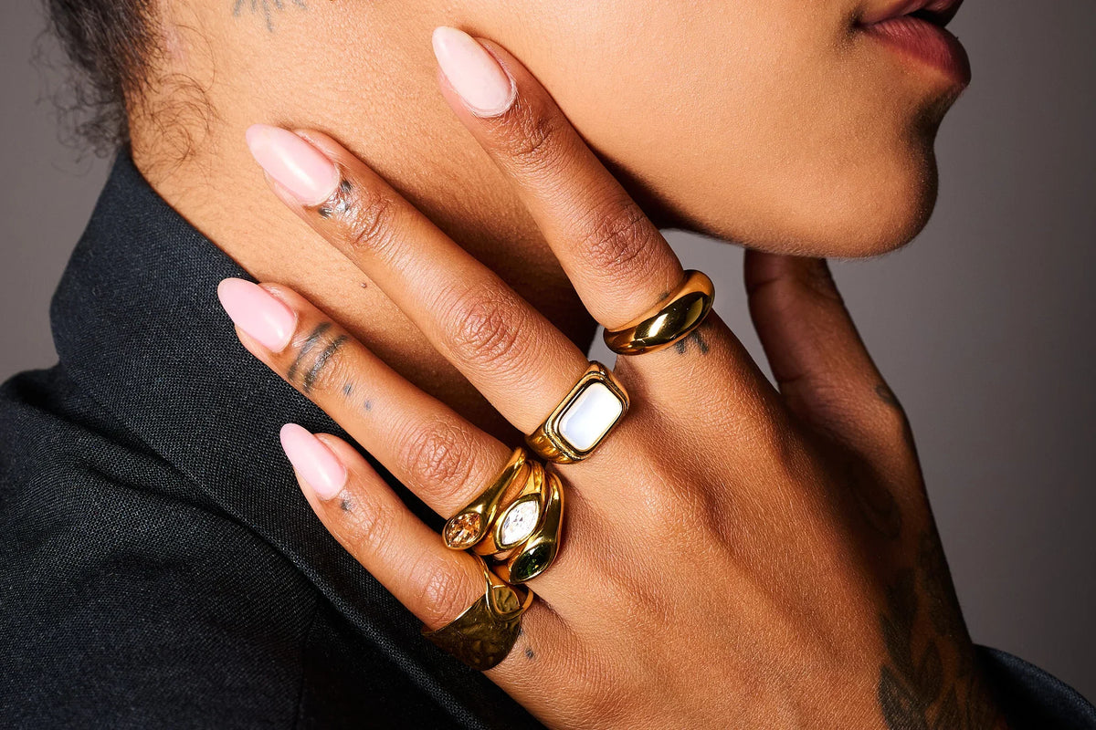 Hand with pink nails wearing multiple gold statement rings and gemstone rings