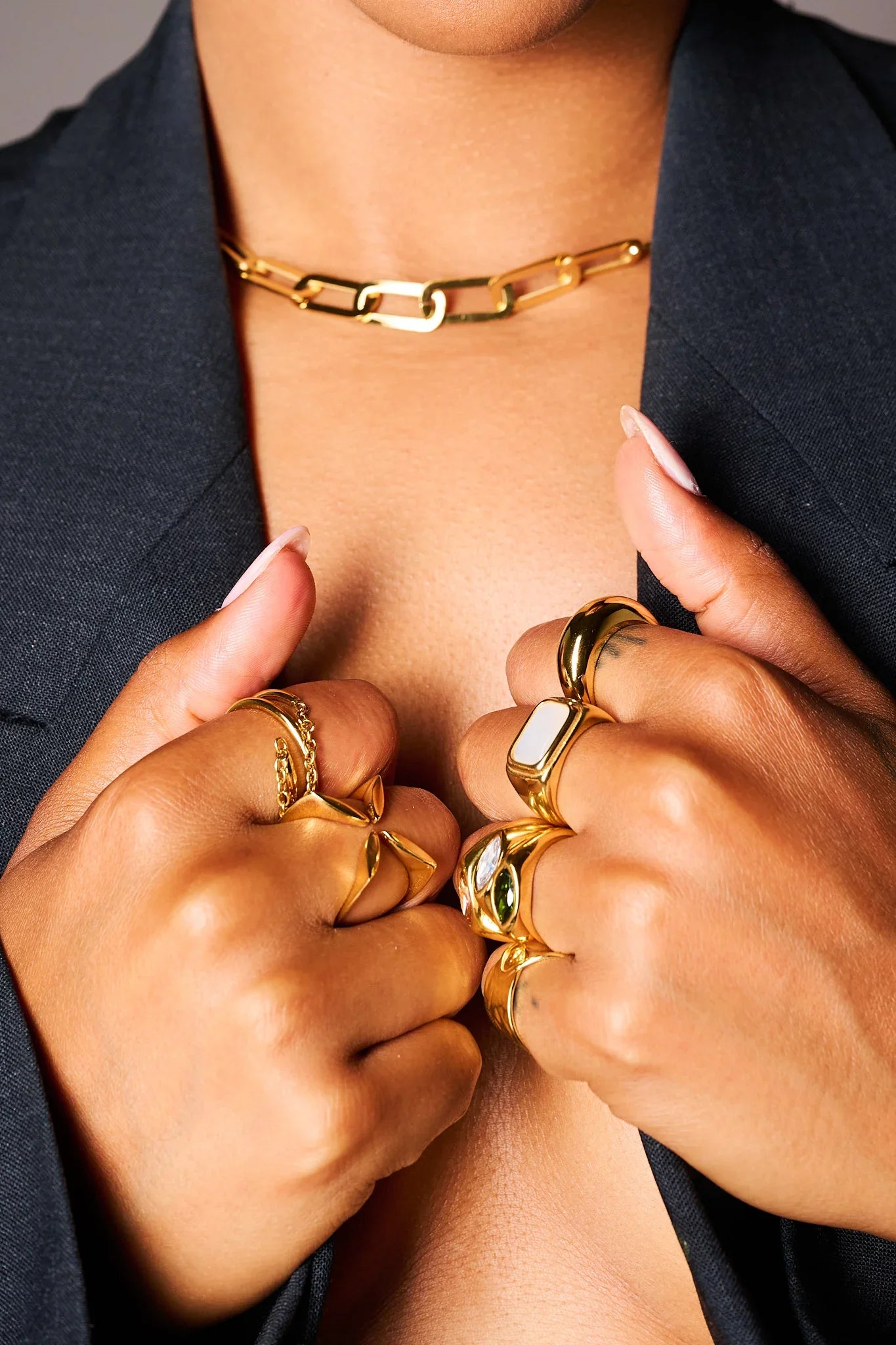 Woman wearing chunky gold rings and a gold chain necklace with black blazer