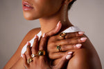 Woman wearing multiple gold rings and a chain drop earring, with manicured nails