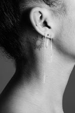 Minimalist silver threader earrings on ear with multiple piercings and sun neck tattoo