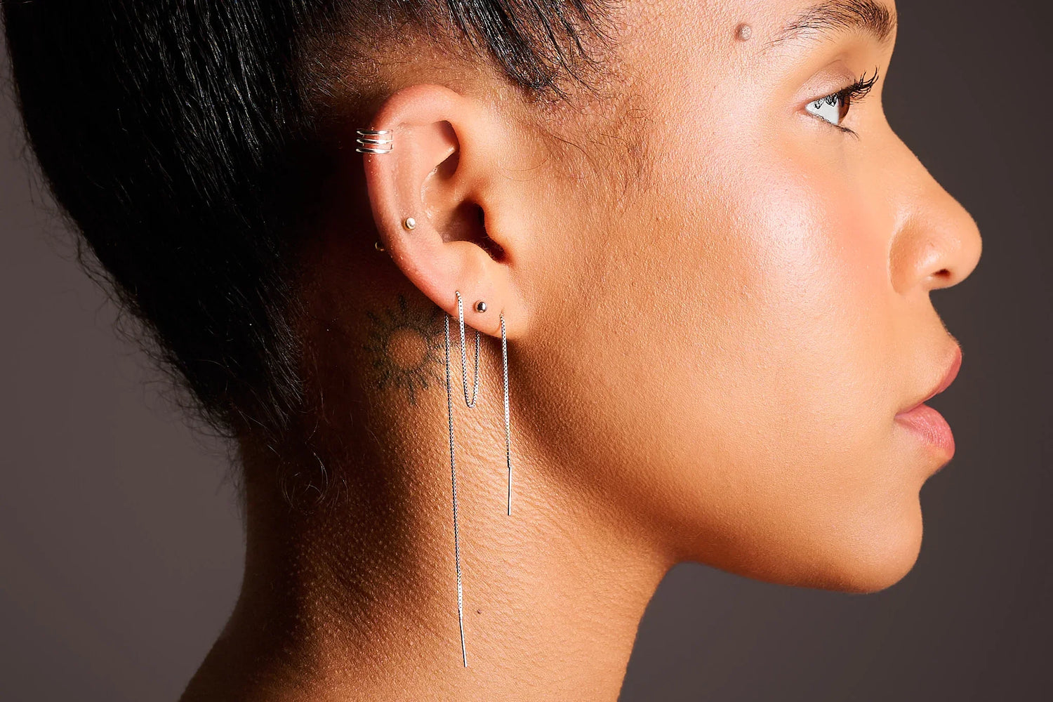 Woman wearing multiple silver earrings, including a long threader earring, close-up