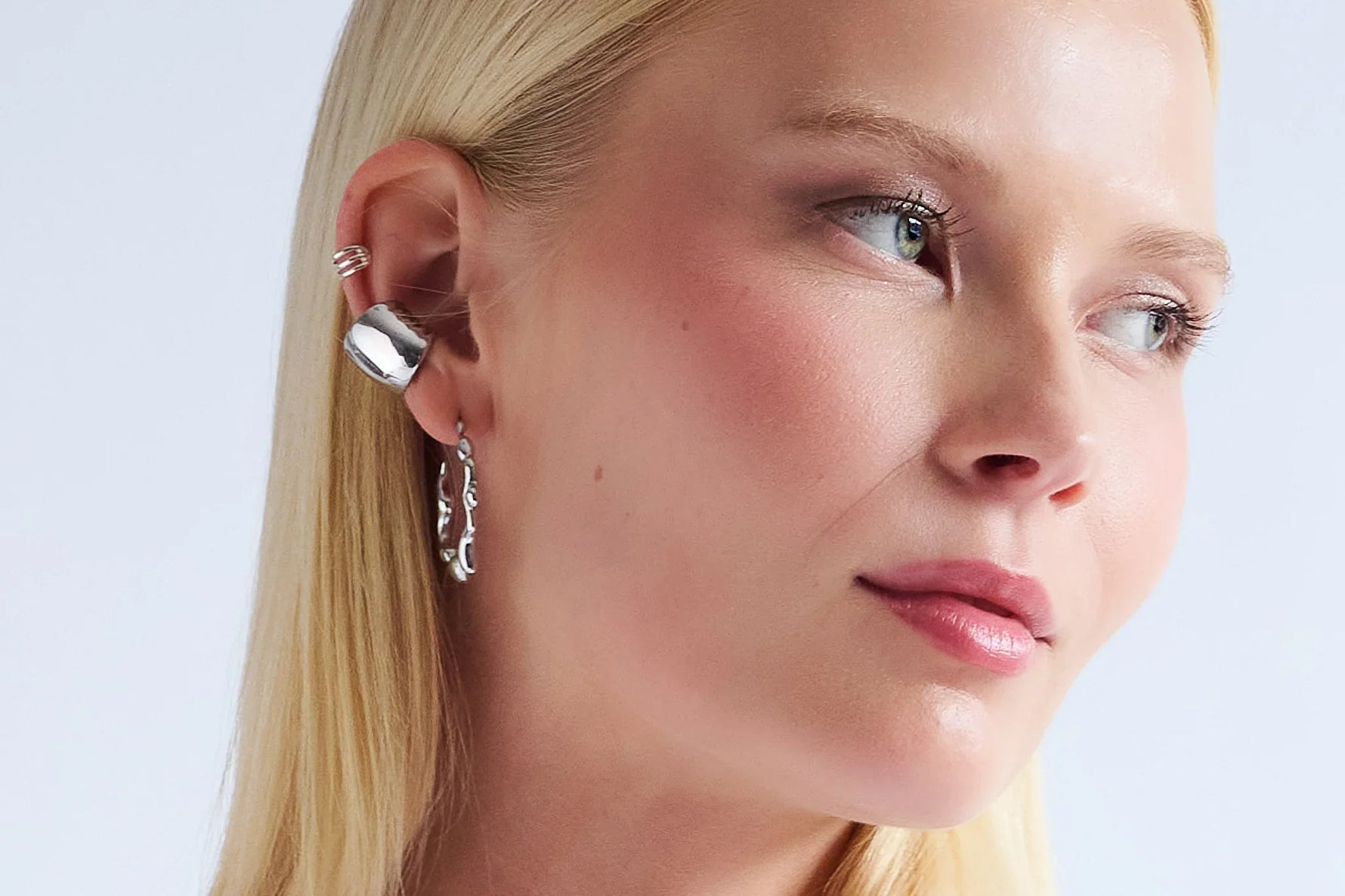 Woman wearing modern silver ear cuff and textured hoop earring, close-up jewelry detail