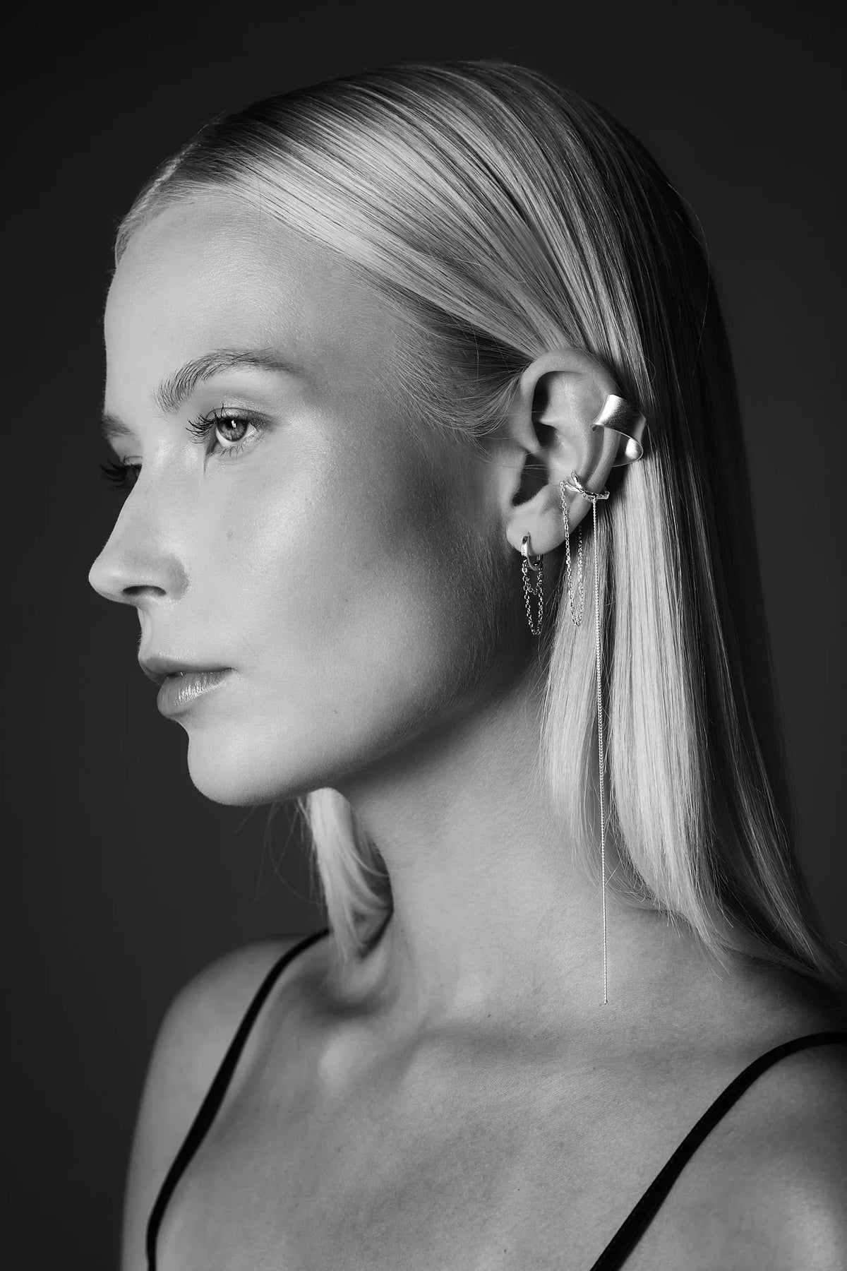 Woman with sleek platinum blonde hair wearing layered silver ear cuffs and chain earrings