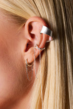 Close-up of a woman's ear wearing multiple silver ear cuffs and chain earrings
