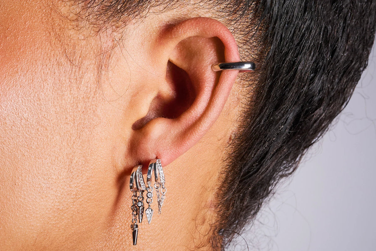 Close-up of ear wearing multiple silver hoop earrings with dangling charms