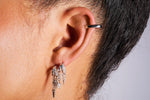 Close-up of ear wearing multiple silver hoop earrings with dangling charms