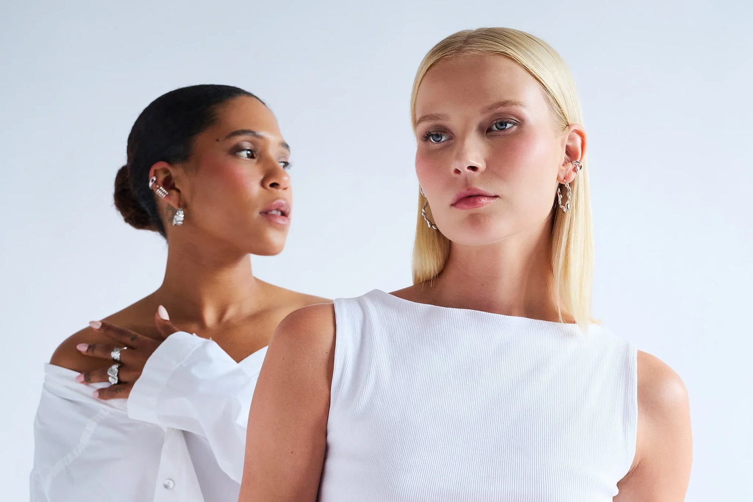 Two women wearing elegant earrings and rings, showcasing modern fine jewellery against a white background.