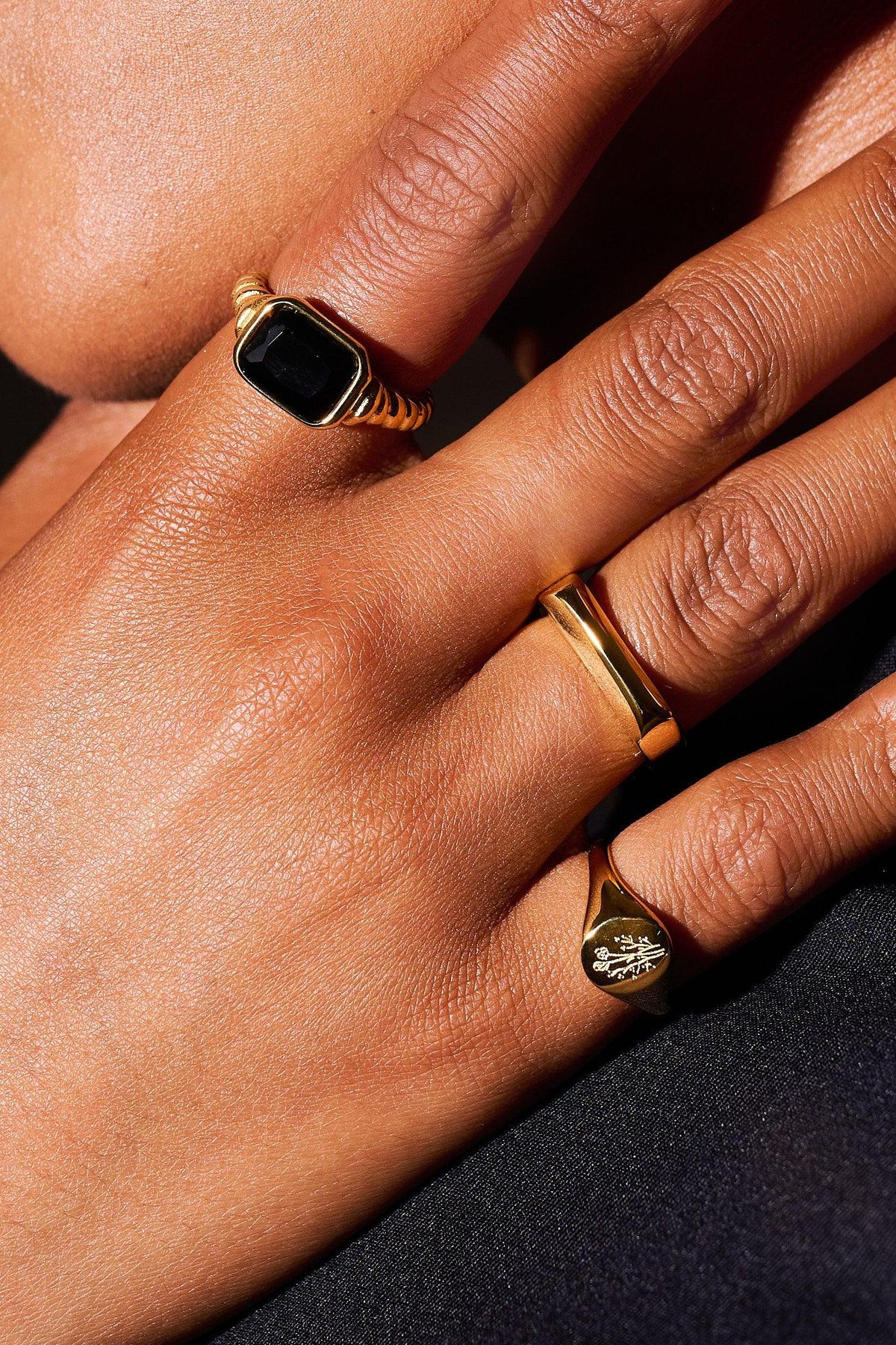 Close-up hand wearing three gold rings with black gemstone and engraved floral detail