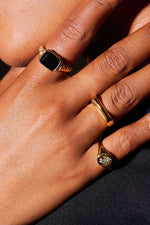 Close-up hand wearing three gold rings with black gemstone and engraved floral detail
