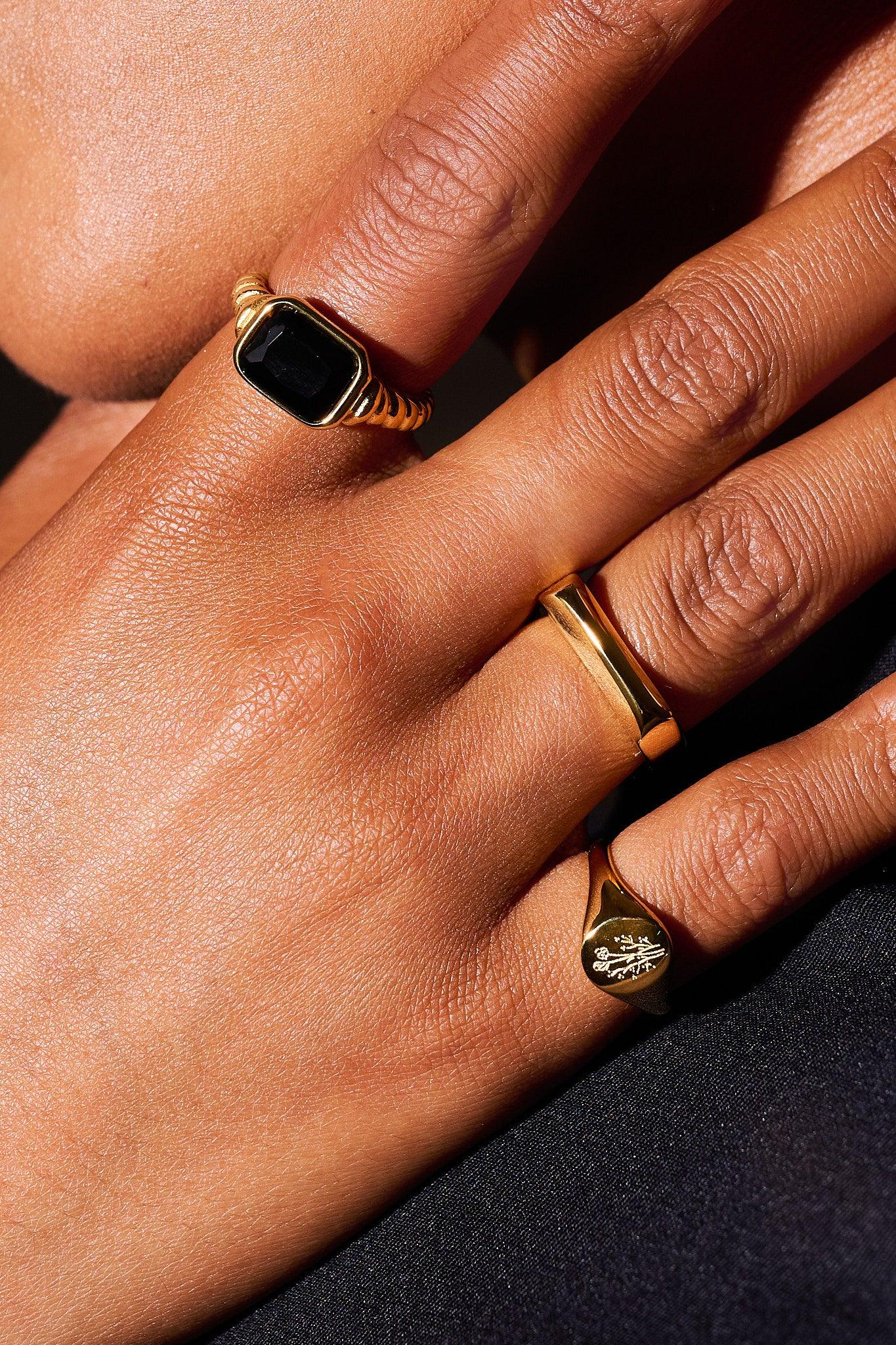 Close-up hand wearing three gold rings with black gemstone and engraved floral detail