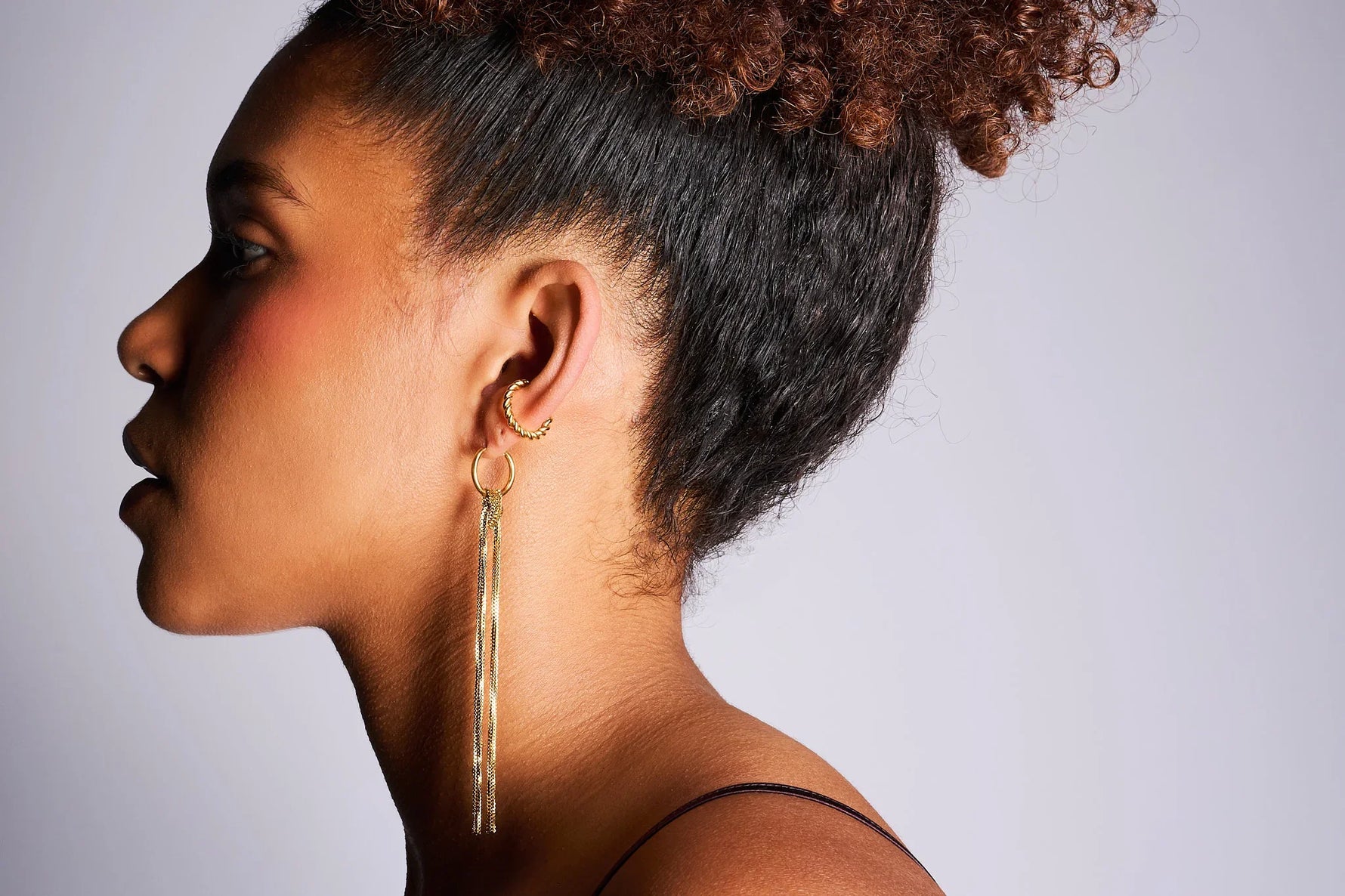 Woman wearing gold hoop earrings with long chain tassels and twisted ear cuff