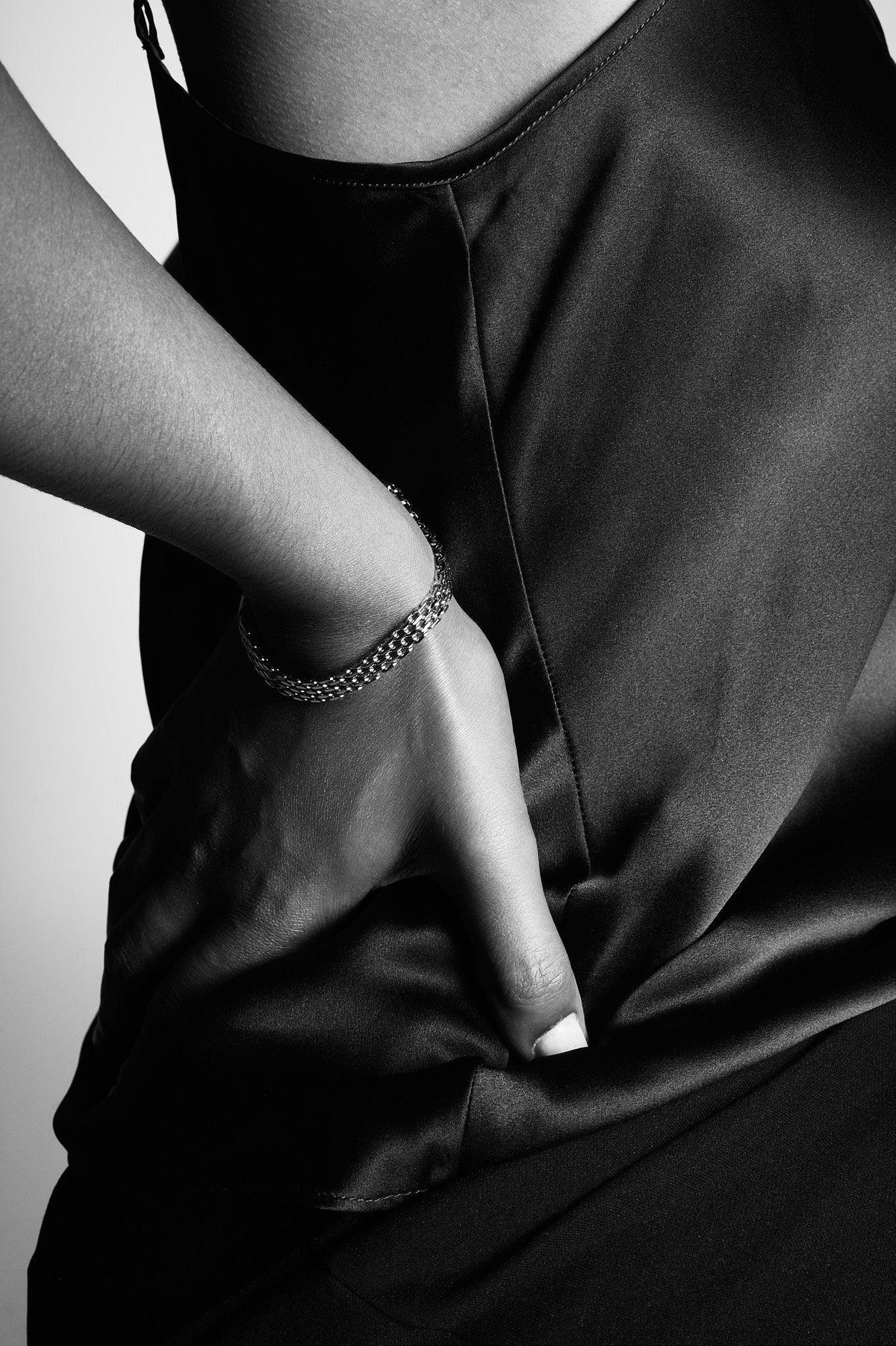 Close-up of a woman's hand wearing a silver chain bracelet on a satin dress