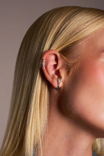 Woman with blonde hair wearing modern silver ear cuff and twisted silver hoop earring