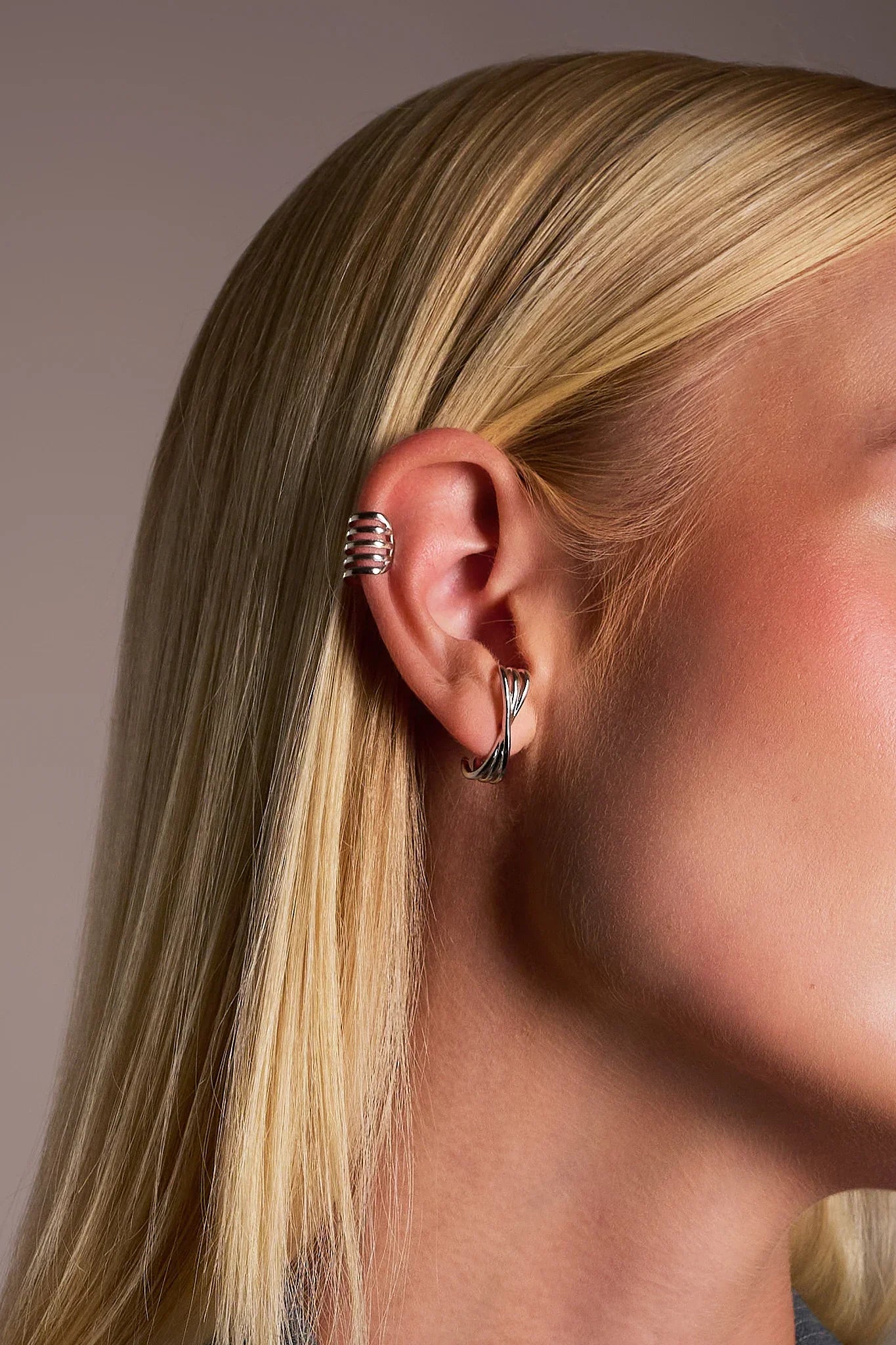 Woman with blonde hair wearing modern silver ear cuff and twisted silver hoop earring