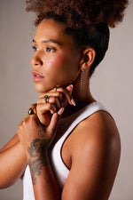 Woman wearing gold rings and chain drop earring, with tattooed hand and white sleeveless top