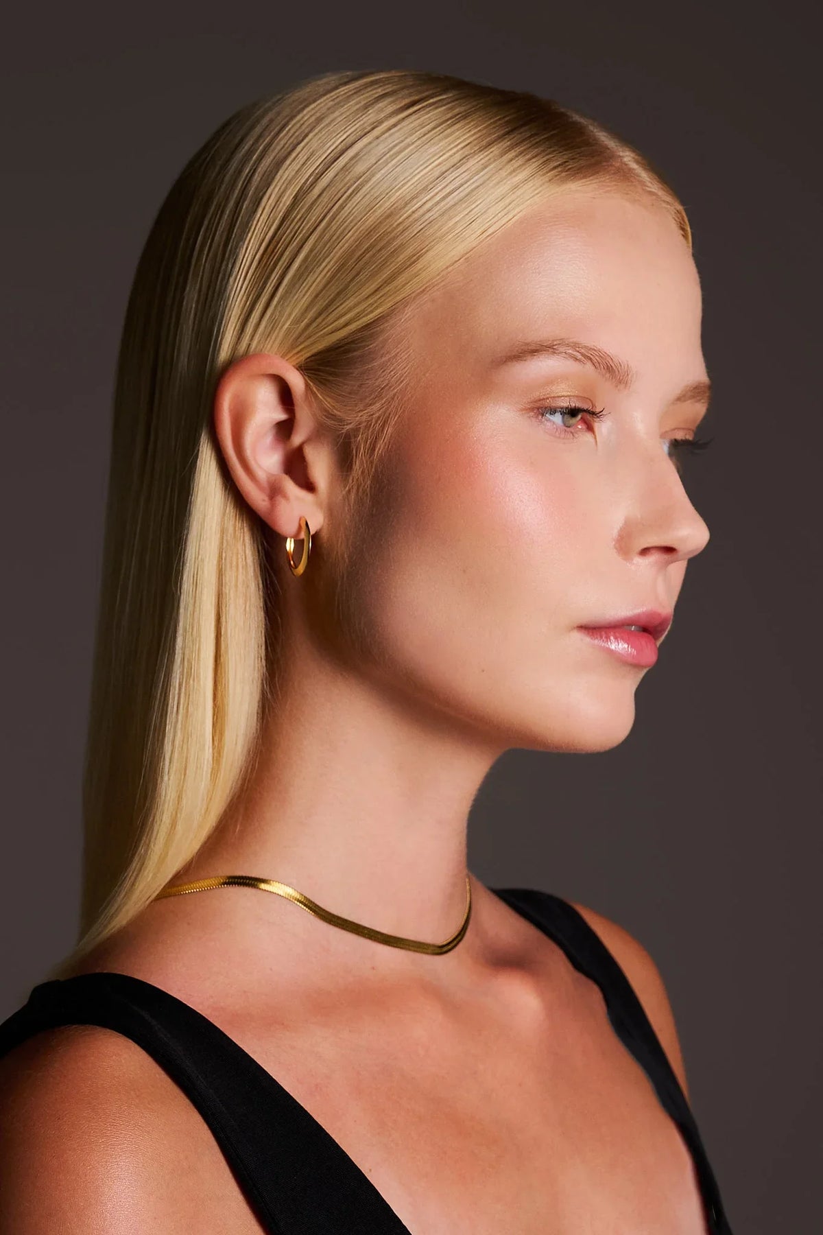 Woman wearing sleek gold hoop earrings and a gold necklace, minimalist jewelry style
